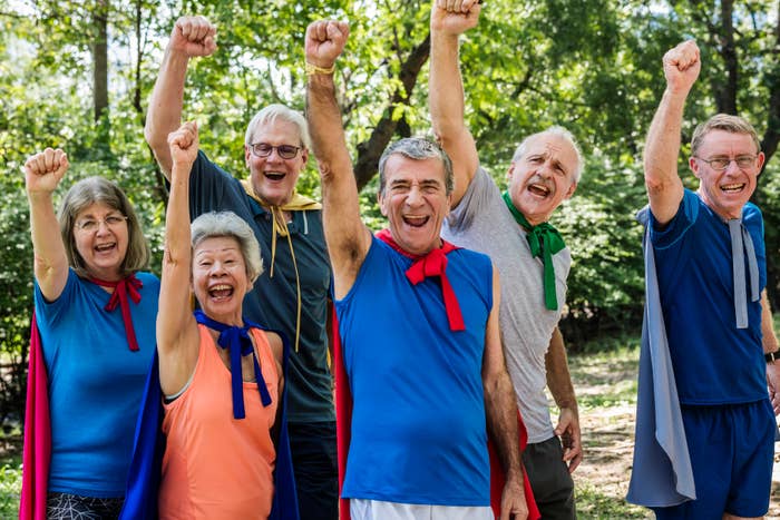 Six older people joyfully raising fists in triumph, wearing casual athleticwear with ribbons around necks, standing outdoors