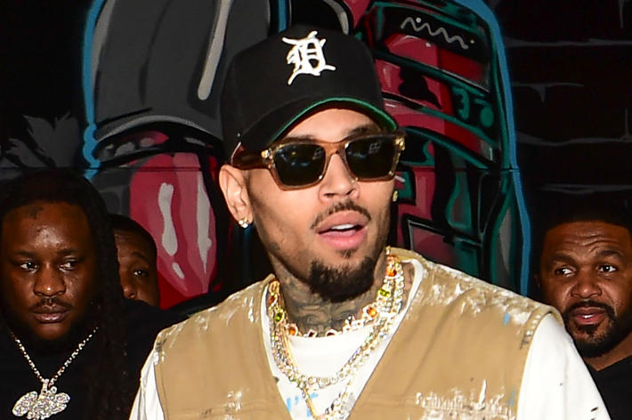 Chris Brown wearing a hat and a gold chain, with people in the background