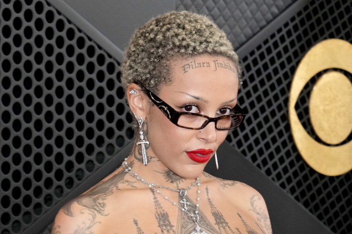 Doja Cat with a buzz cut, detailed tattoos, diamond jewelry, and a silver chain top at the Grammys