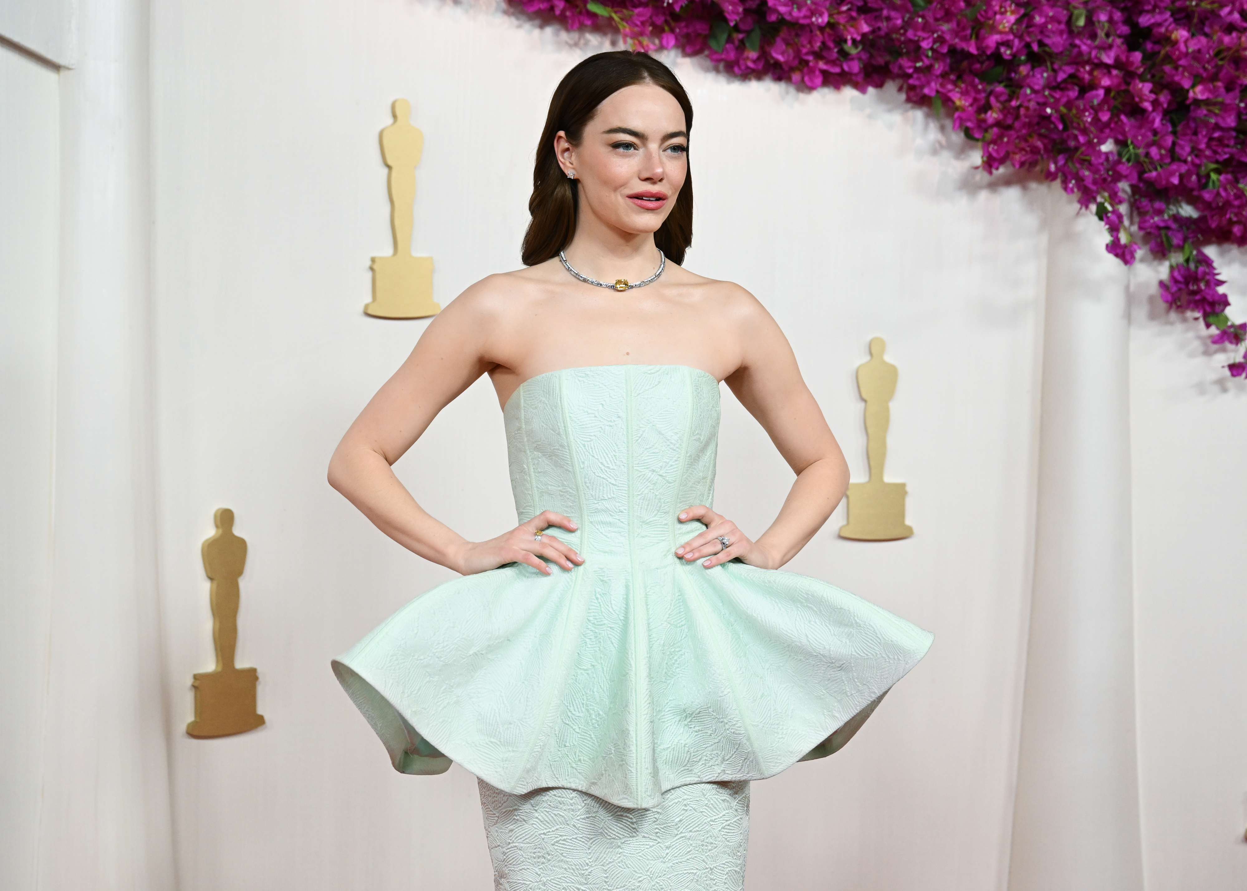 Emma Stone at the Oscars posing on the red carpet with her hands on her hips