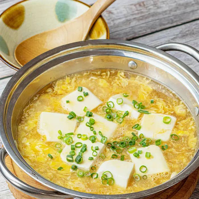 鍋に入った豆腐と卵の入った味噌汁、トッピングにネギが散らされている。