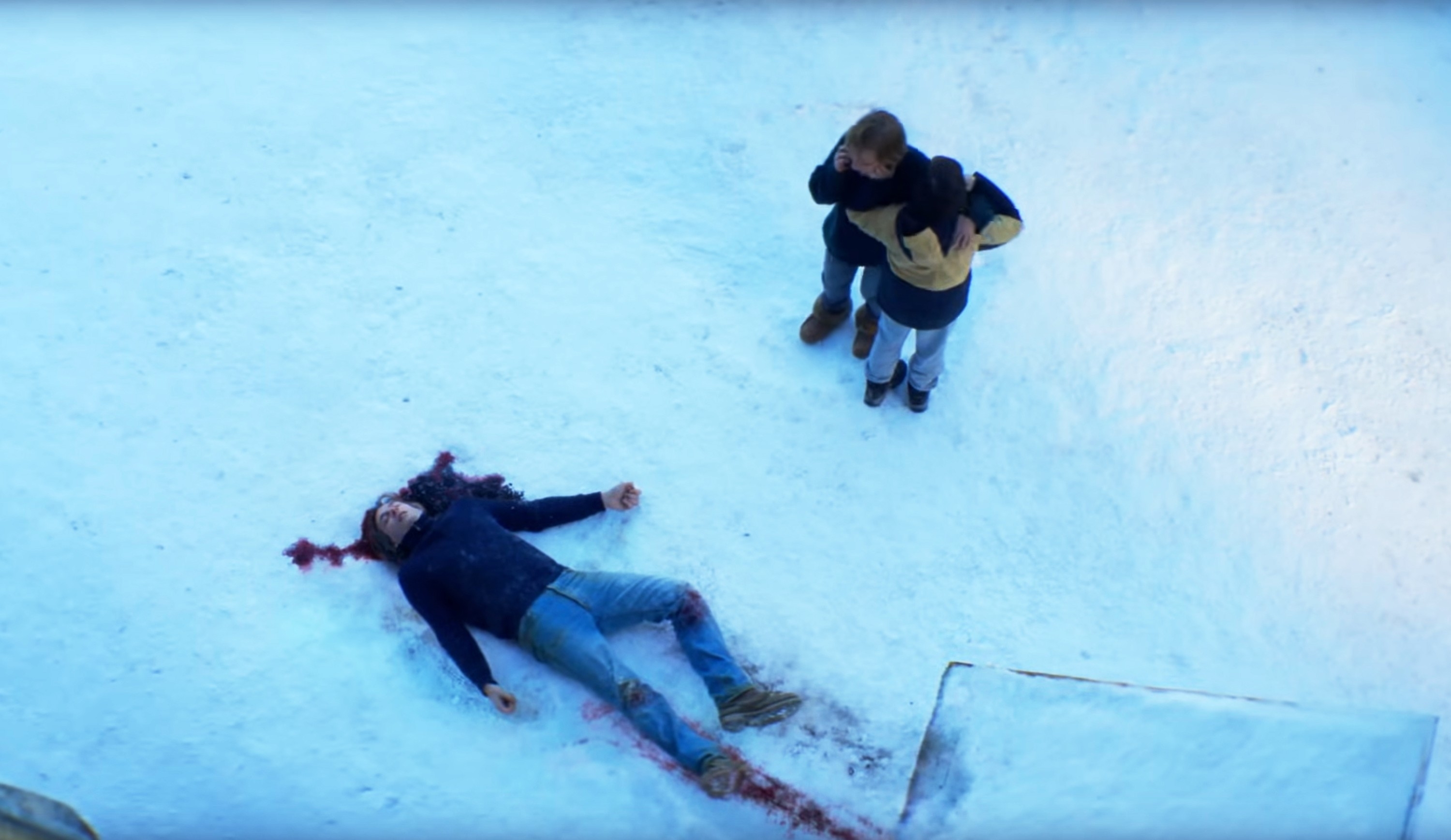 Two people stand by a dead bloody body in the snow
