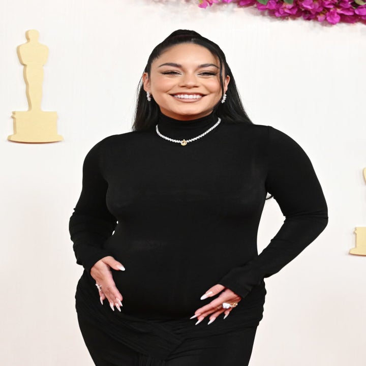 A pregnant celebrity in a black outfit smiles at an event with Oscar statues and flowers in the background