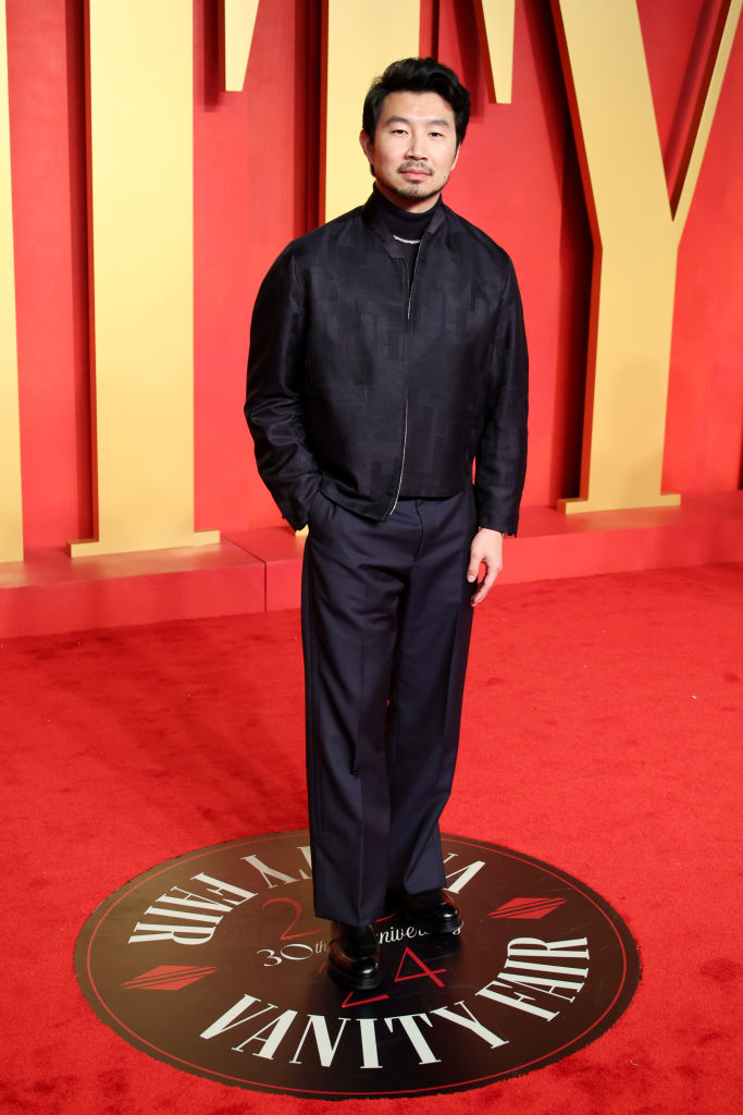 Simu on red carpet in black jacket, turtleneck, and trousers, hands in pockets