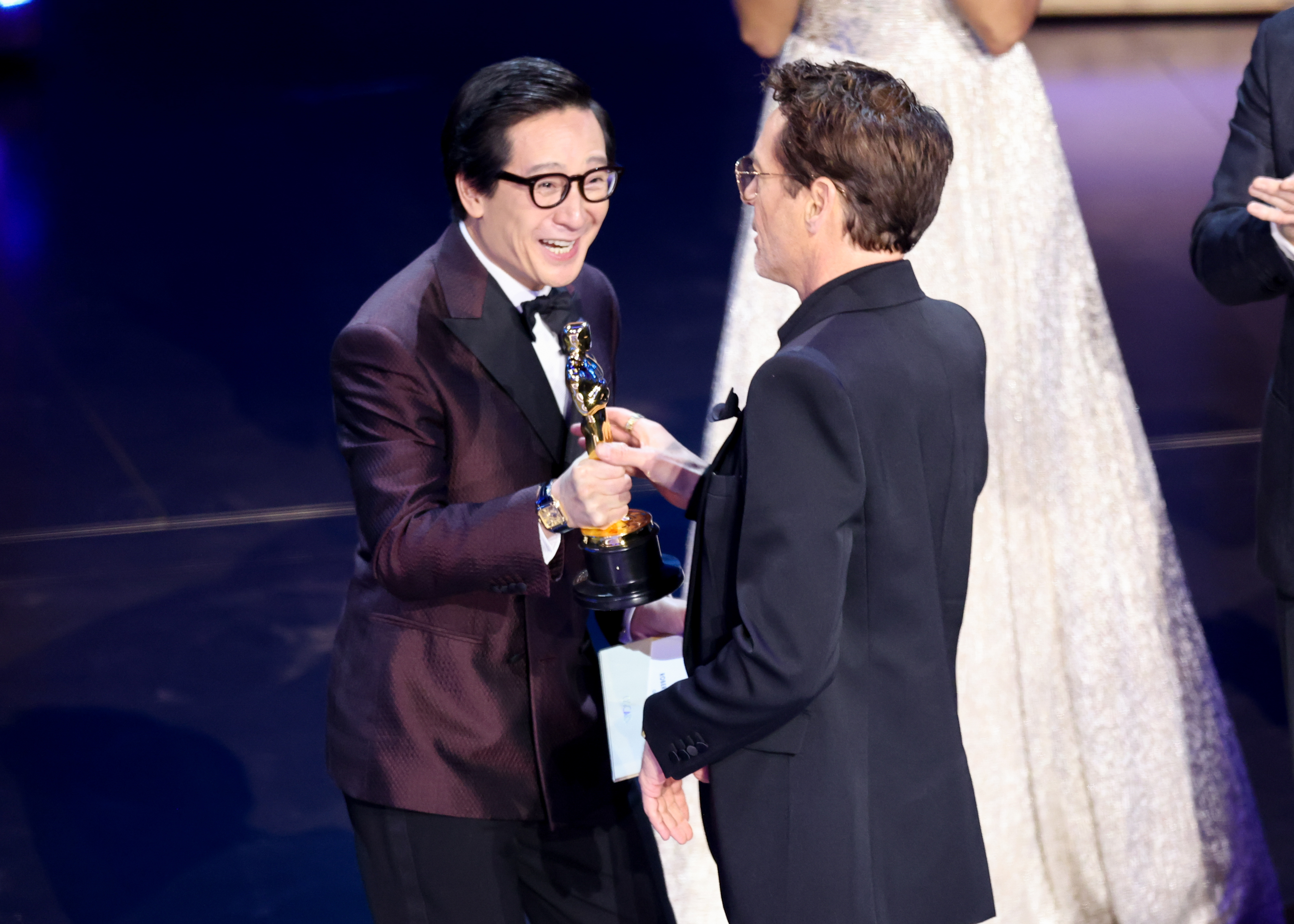 Ke Huy smiling at RDJ onstage and presenting the Oscar statuette to him