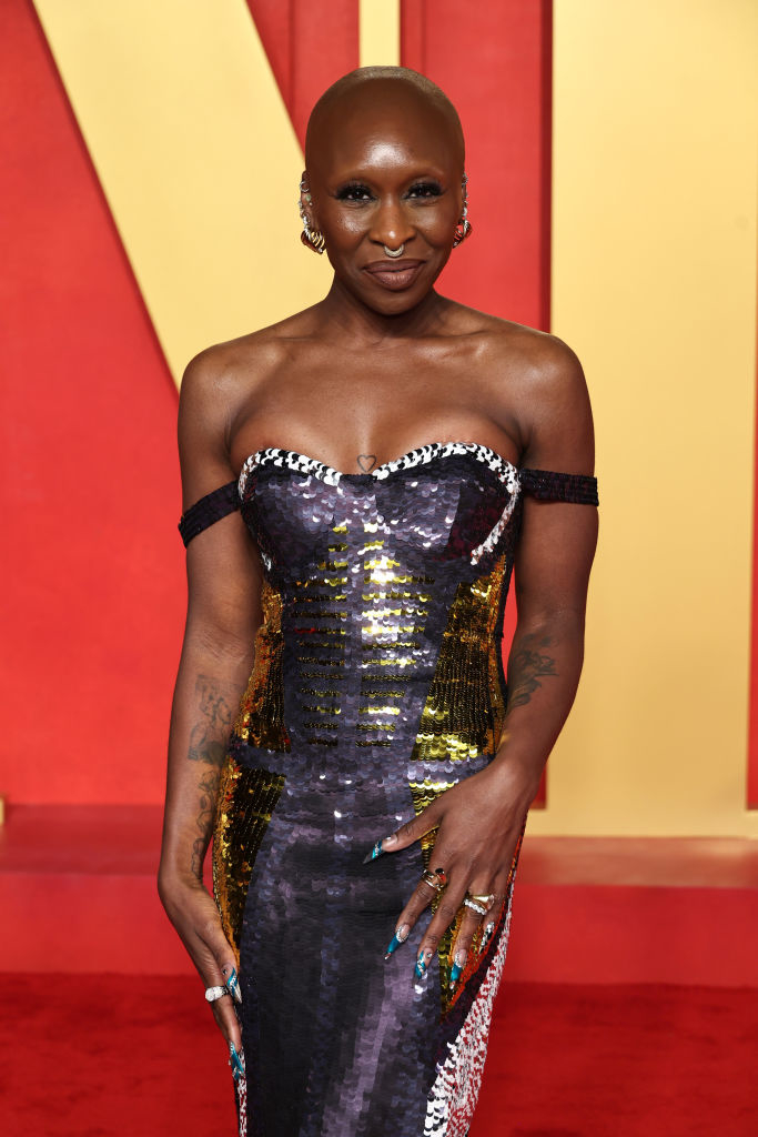Cynthia poses on the red carpet in a sequined off-the-shoulder dress with her hands on her hips