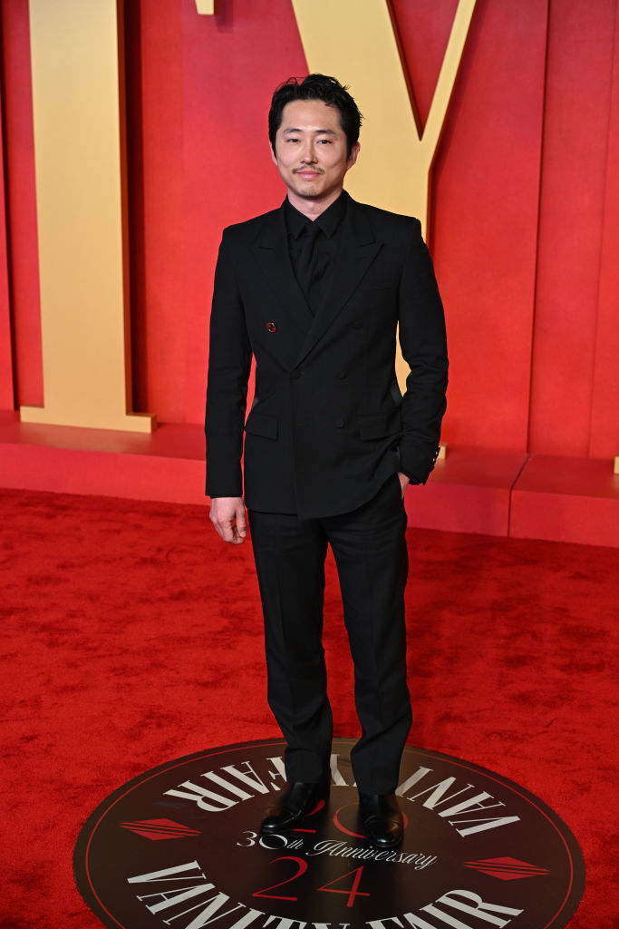 Steven stands on a red carpet at an event, wearing a formal black suit with a boutonniere