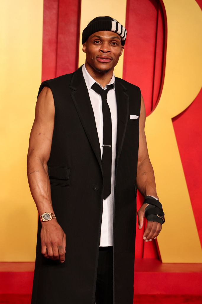 Russell in a sleeveless tuxedo with tie and a cap with a wrist brace