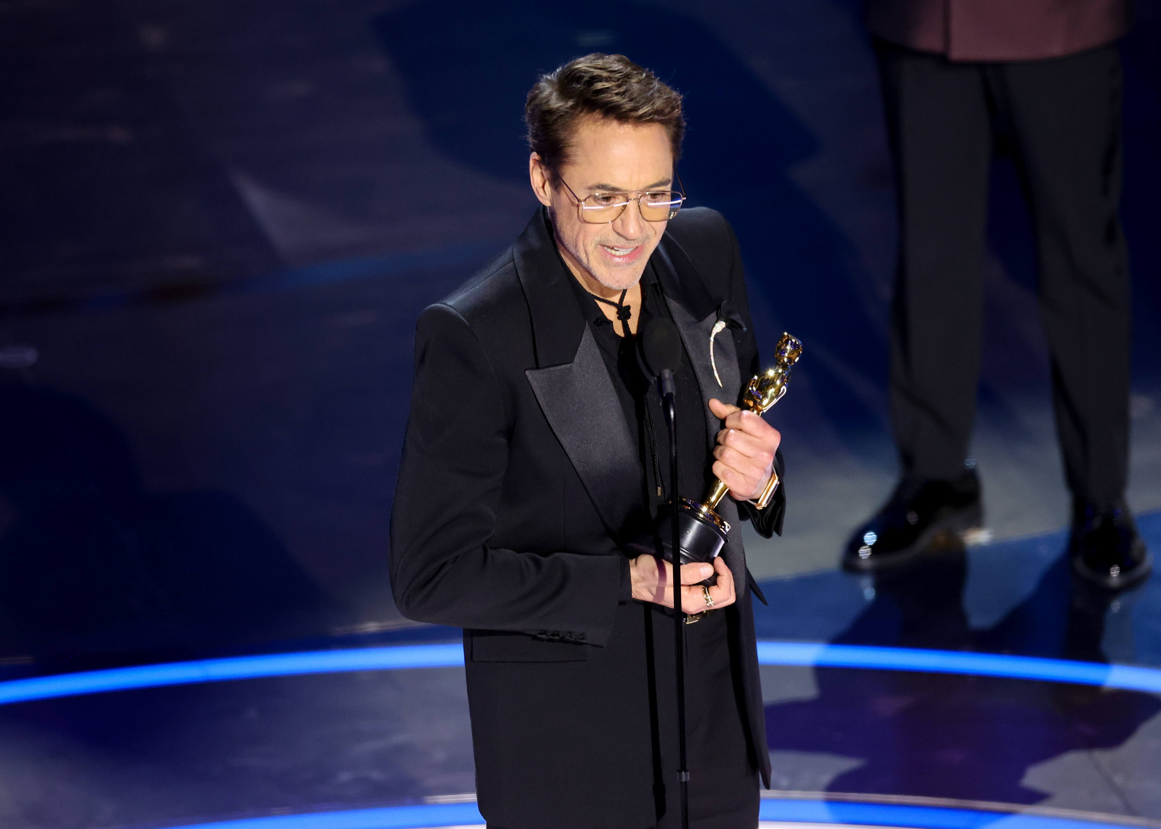 RDJ in a suit holding an Oscar onstage