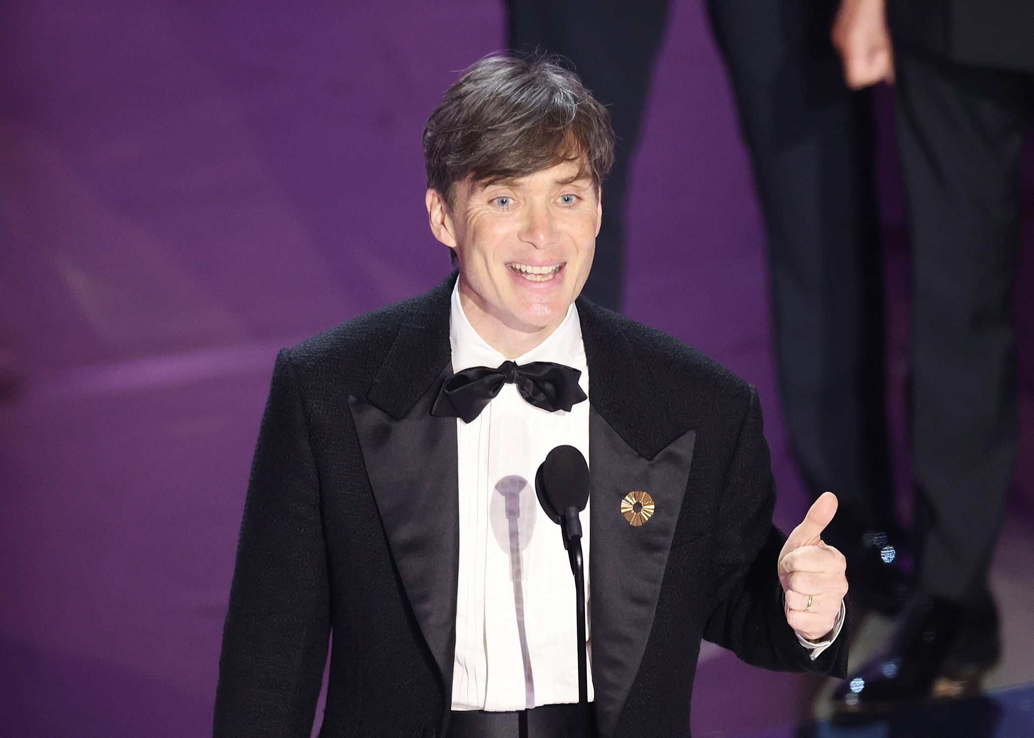 Cillian smiling onstasge in a tuxedo with a bow tie giving a thumbs-up