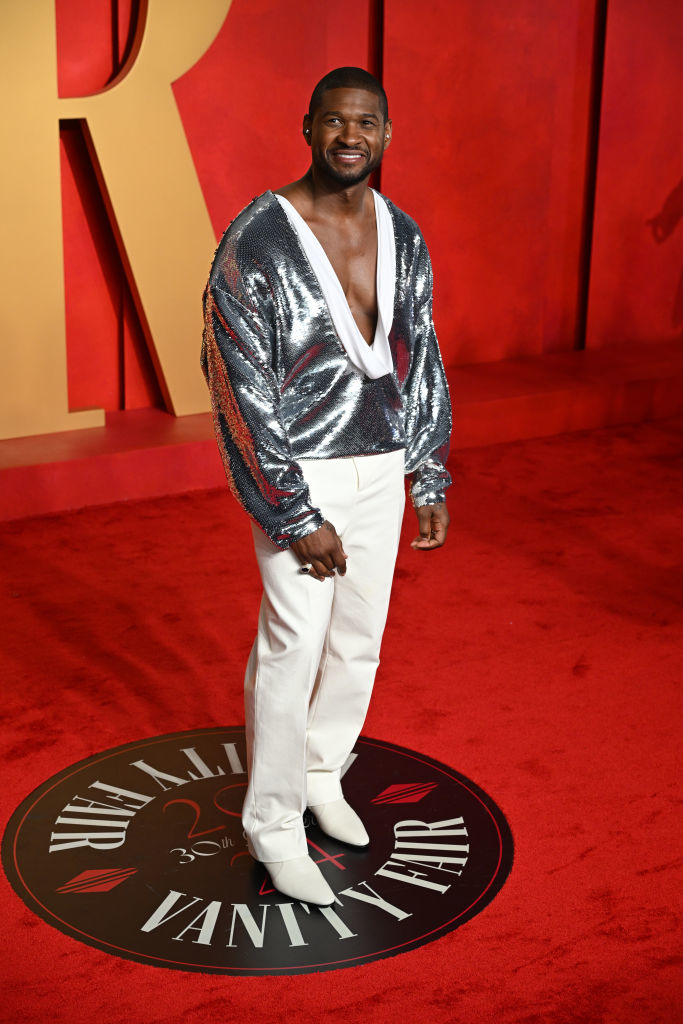Usher in a silver jacket and white pants smiles on the red carpet