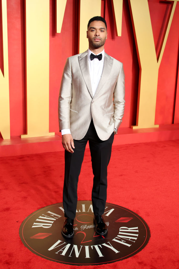 Regé-Jean in a silver blazer and black trousers with bow tie stands on Vanity Fair carpet