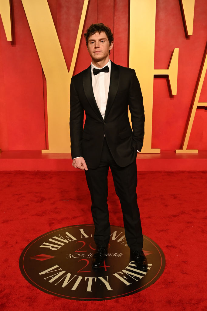 Evan in a black suit and bow tie standing on a Vanity Fair event logo
