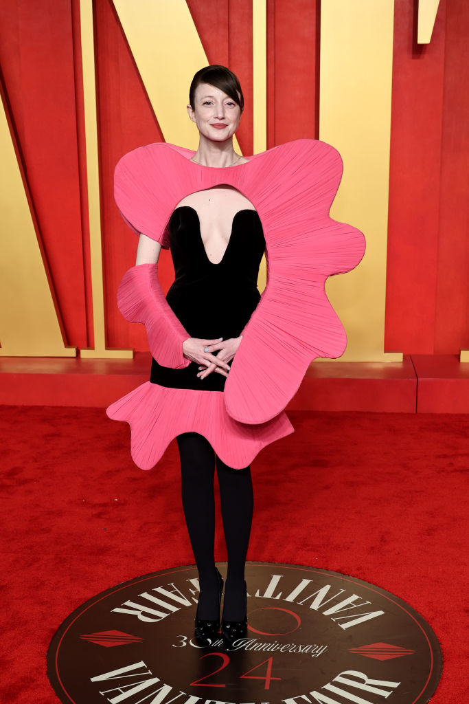 Andrea on the red carpet wearing a large pink flower-shaped outfit with a black center