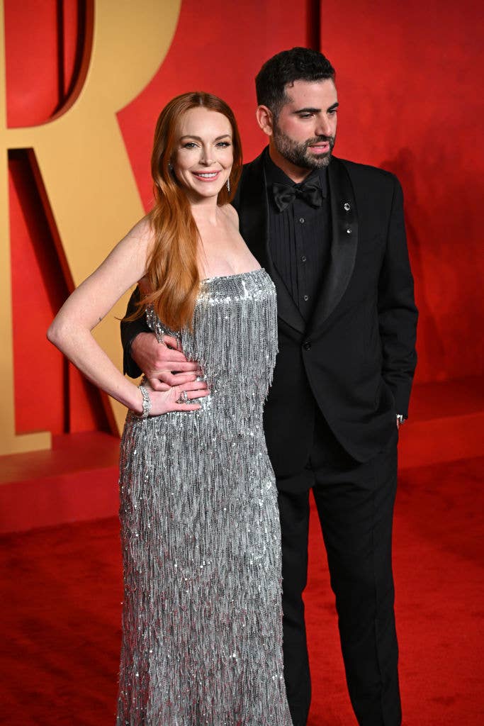 Lindsay Lohan posing on red carpet in a sleeveless, shimmering, full-length gown; Bader, her husband, in a classic black tuxedo