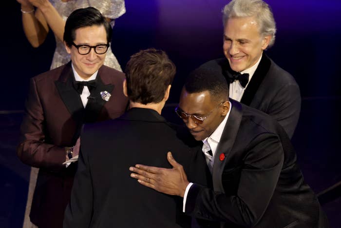 Mahershala hugging RDJ onstage as Christoph and Hu smile and look on