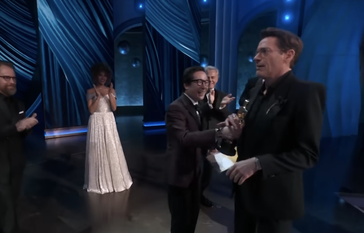 RDJ receives an award onstage from Ke Huy while the others applaud