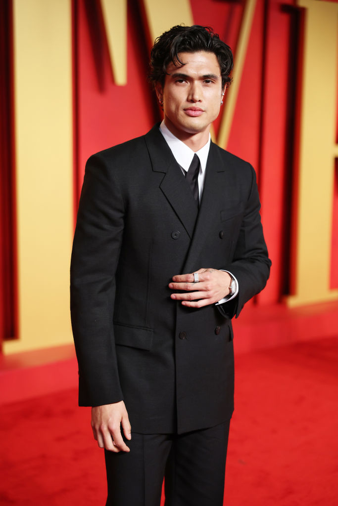 Charles in a classic black suit and tie standing on the red carpet