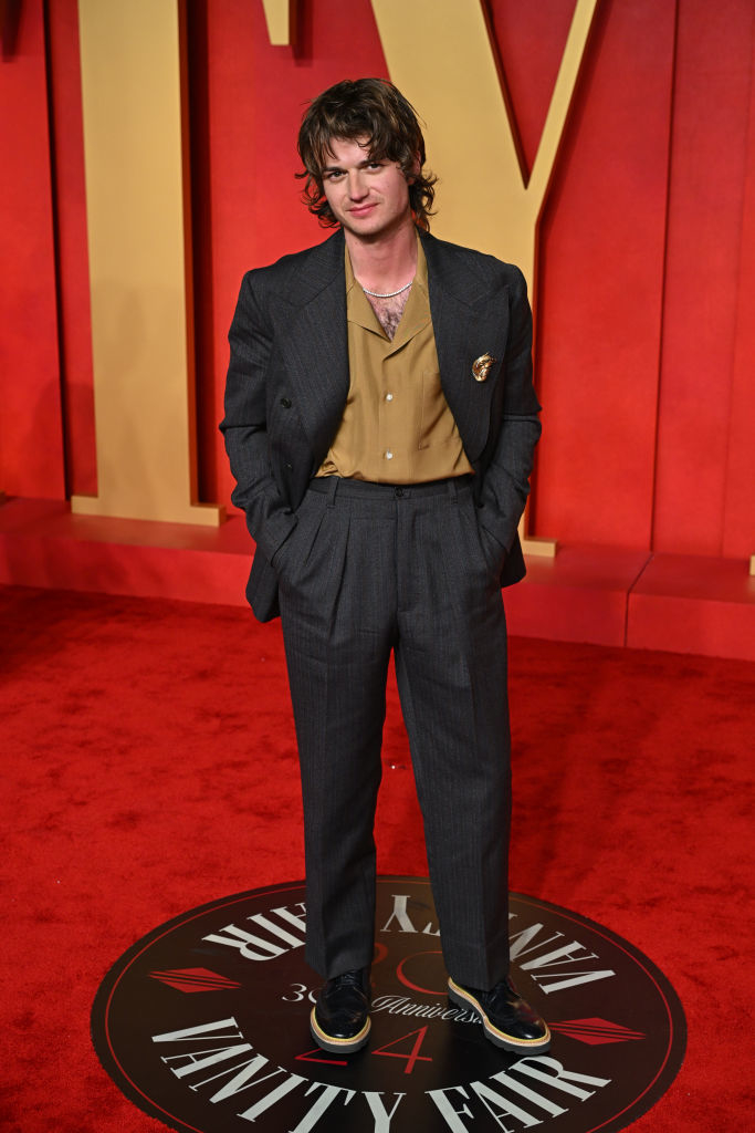 Joe in pin-striped suit and gold shirt stands with hands in pockets on a red carpet event