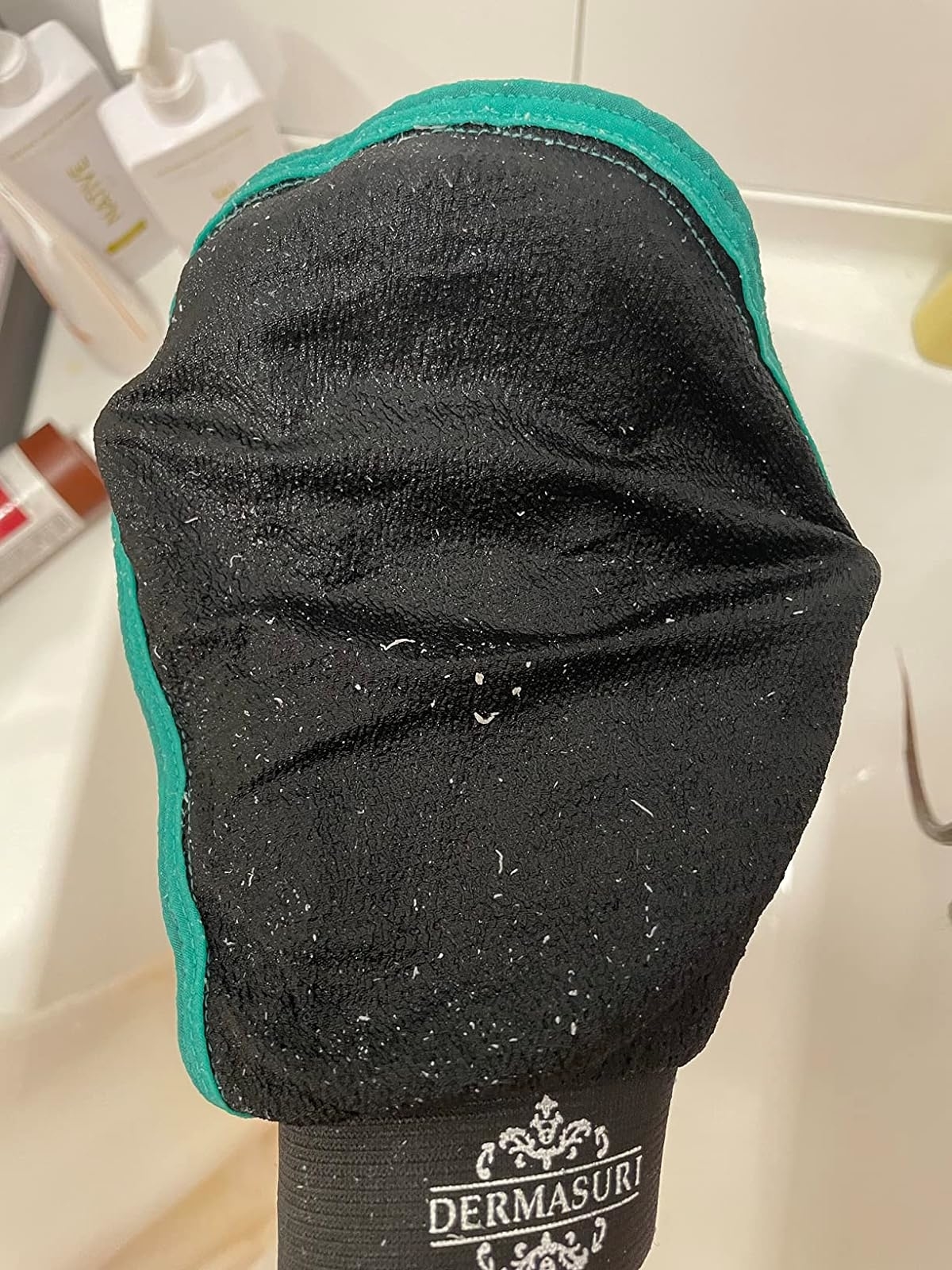 Exfoliating mitt by Dermasuri with visible texture, showing dead skin flakes on it
