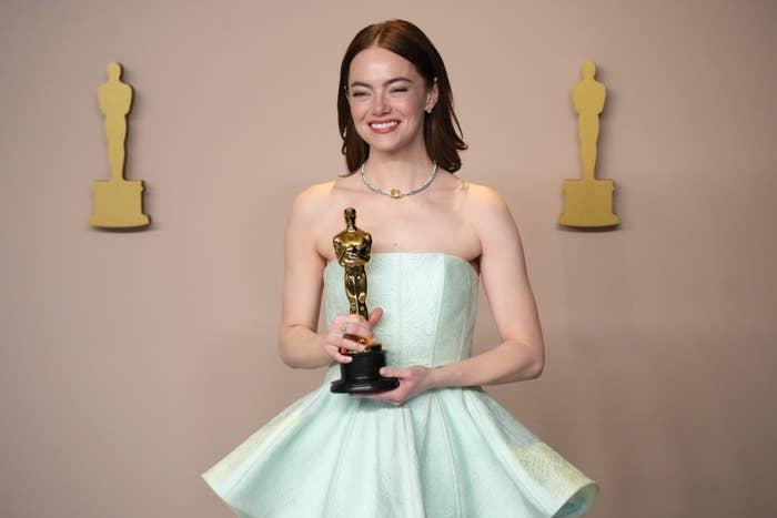Emma Stone in strapless gown holding her Oscar statuette and smiling for photos