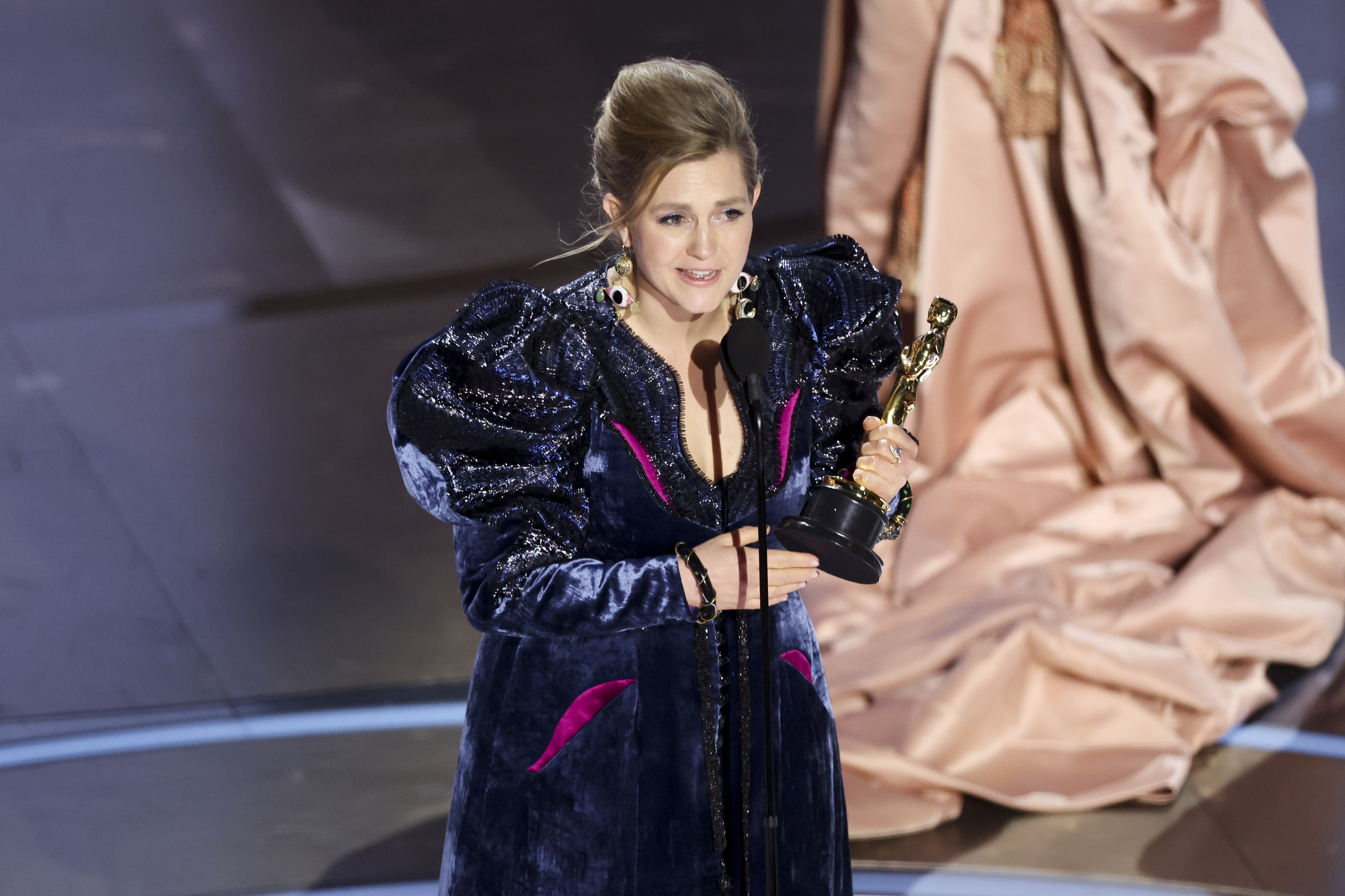 Holly Waddington in embellished outfit holding an Oscar onstage