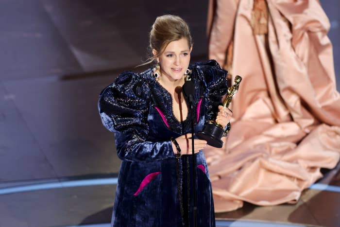 Holly Waddington in embellished outfit holding an Oscar on stage