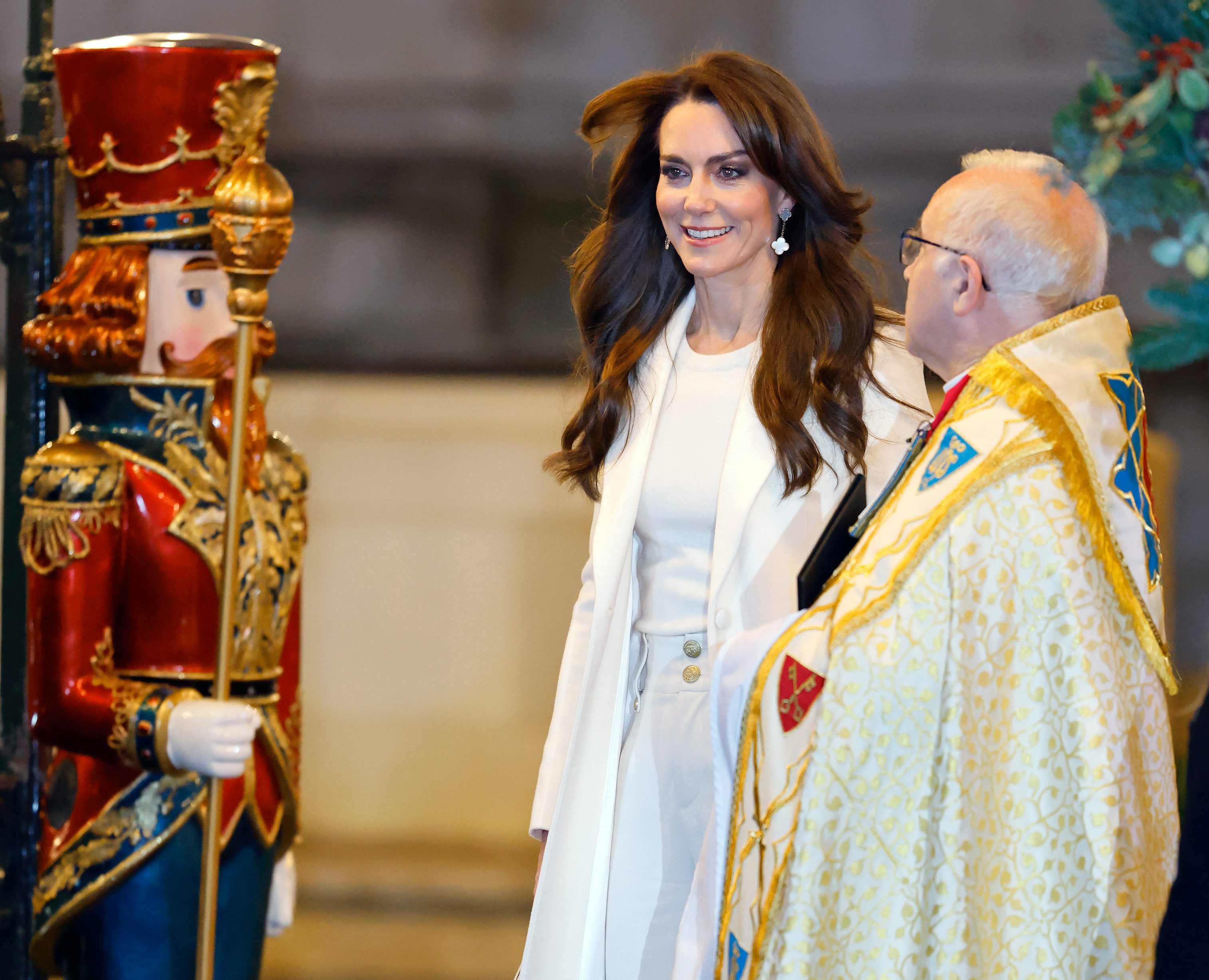 Kate Middleton in a white coat smiling, standing next to a man in ceremonial attire