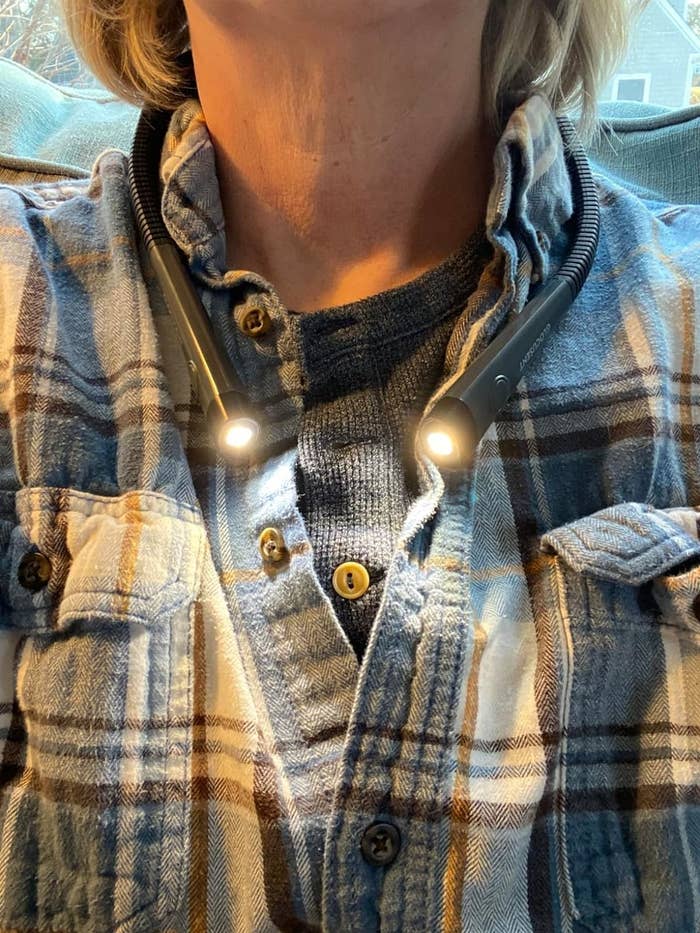 Person wearing a plaid shirt and sweater with a portable neck reading light