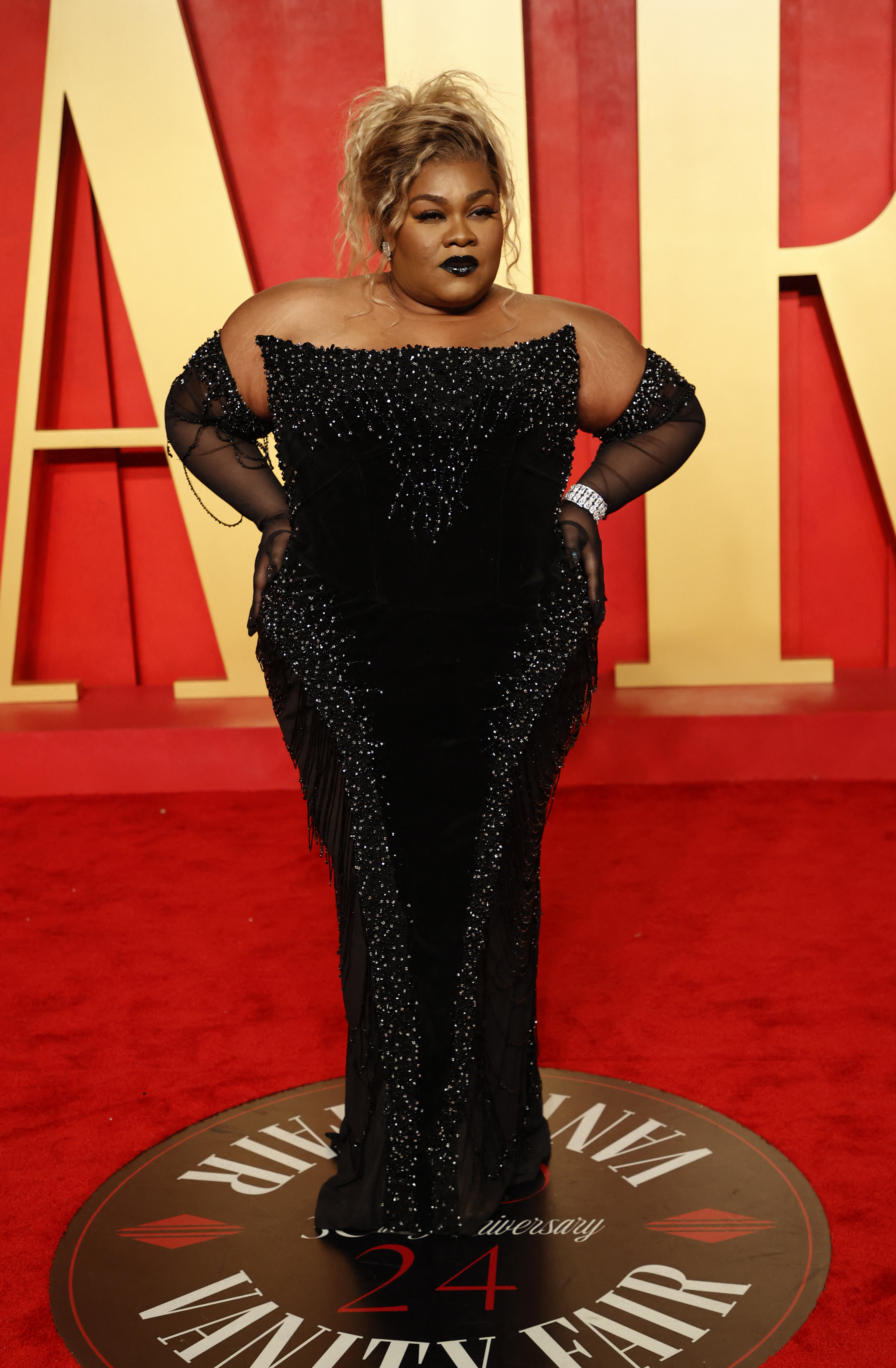 Da&#x27;Vine in a sparkling black off-shoulder gown with sheer sleeves posing on the red carpet