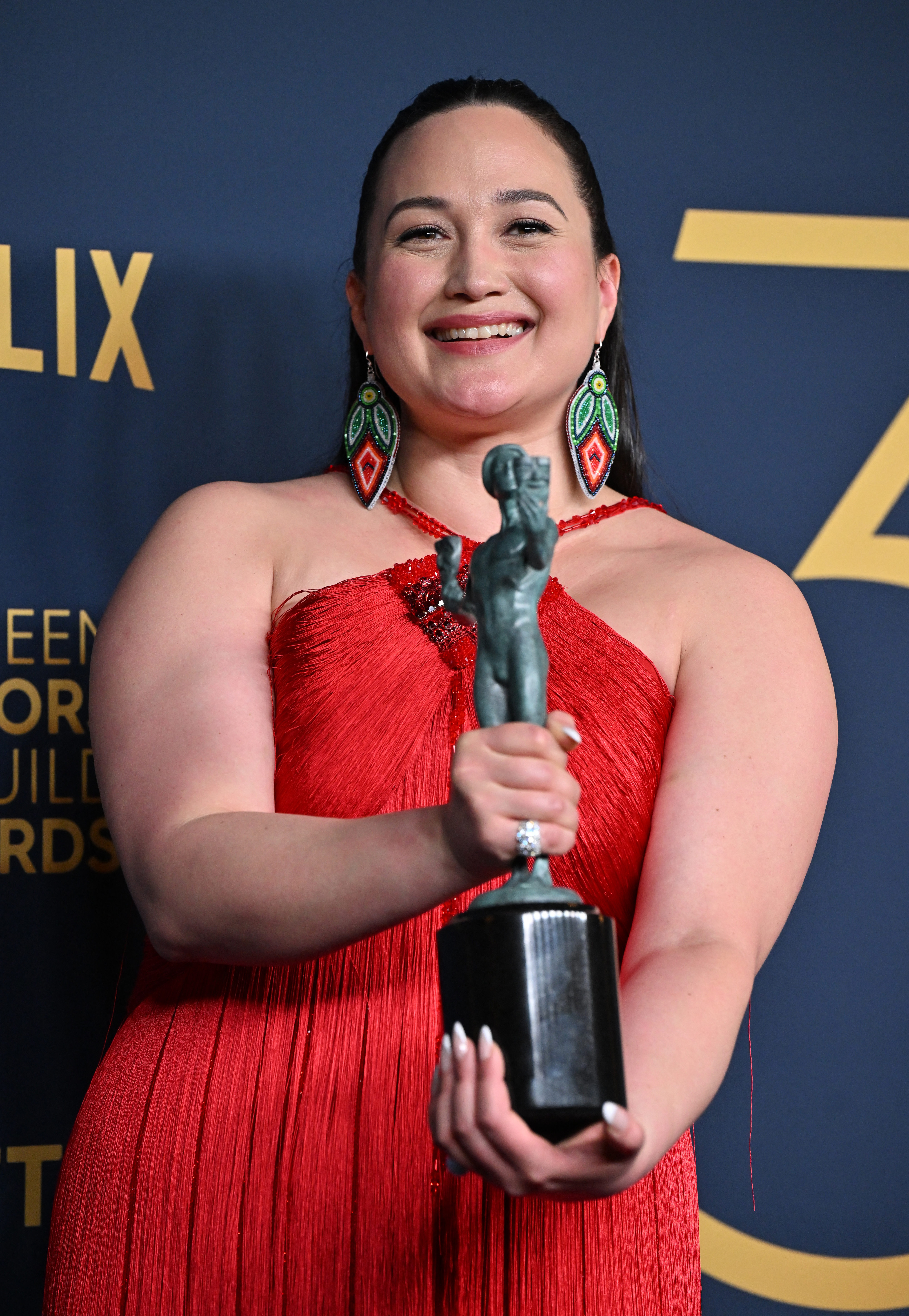 Lily in a pleated gown holding her SAG award and smiling