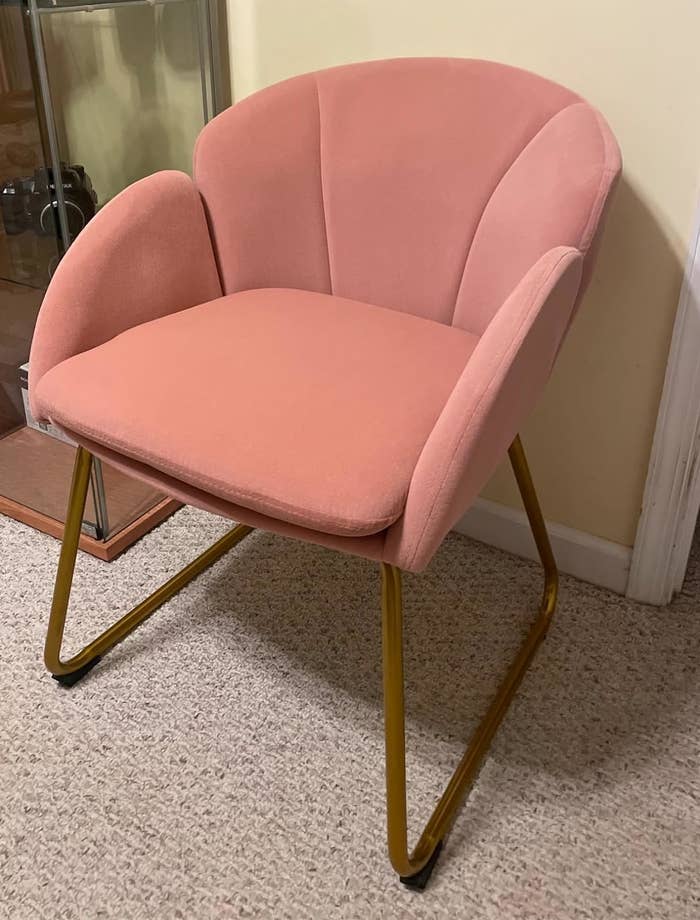 Pink upholstered chair with gold-colored legs on a carpeted floor, suitable for modern home decor