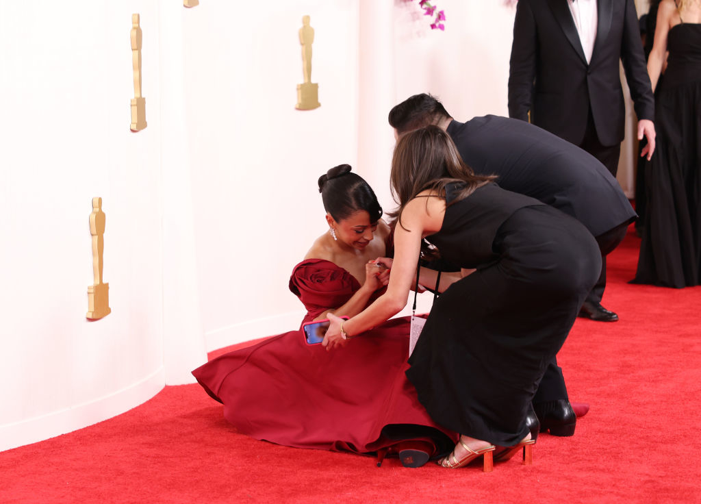Liza in elegant gown being assisted up by two people on the red carpet