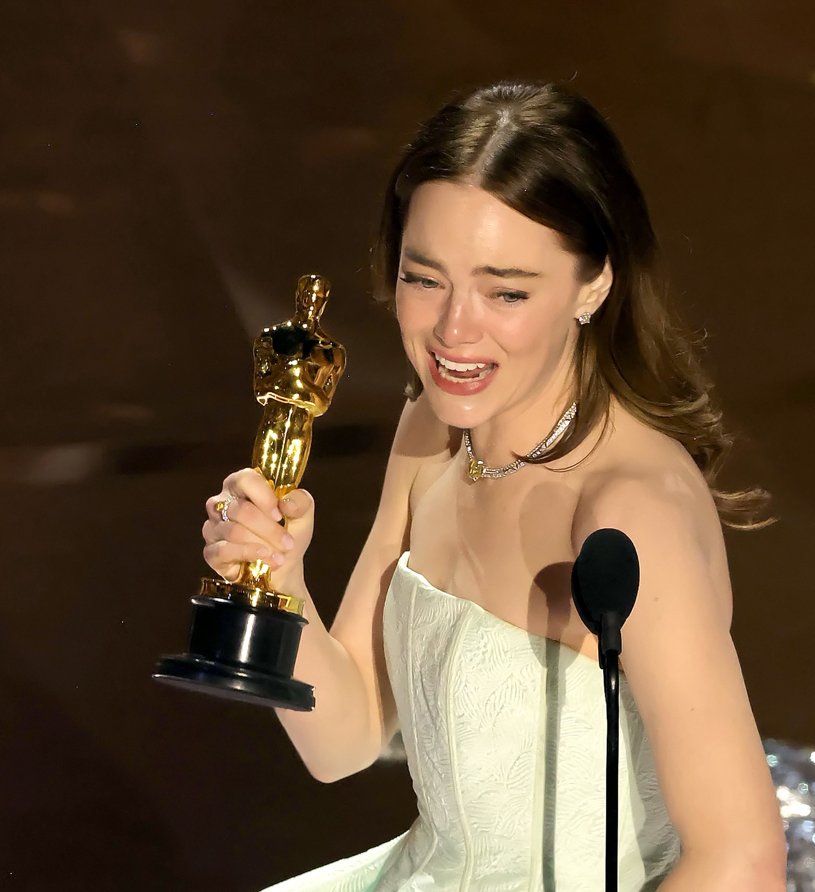 Emma in an evening dress holding an Oscar trophy, expressing joy