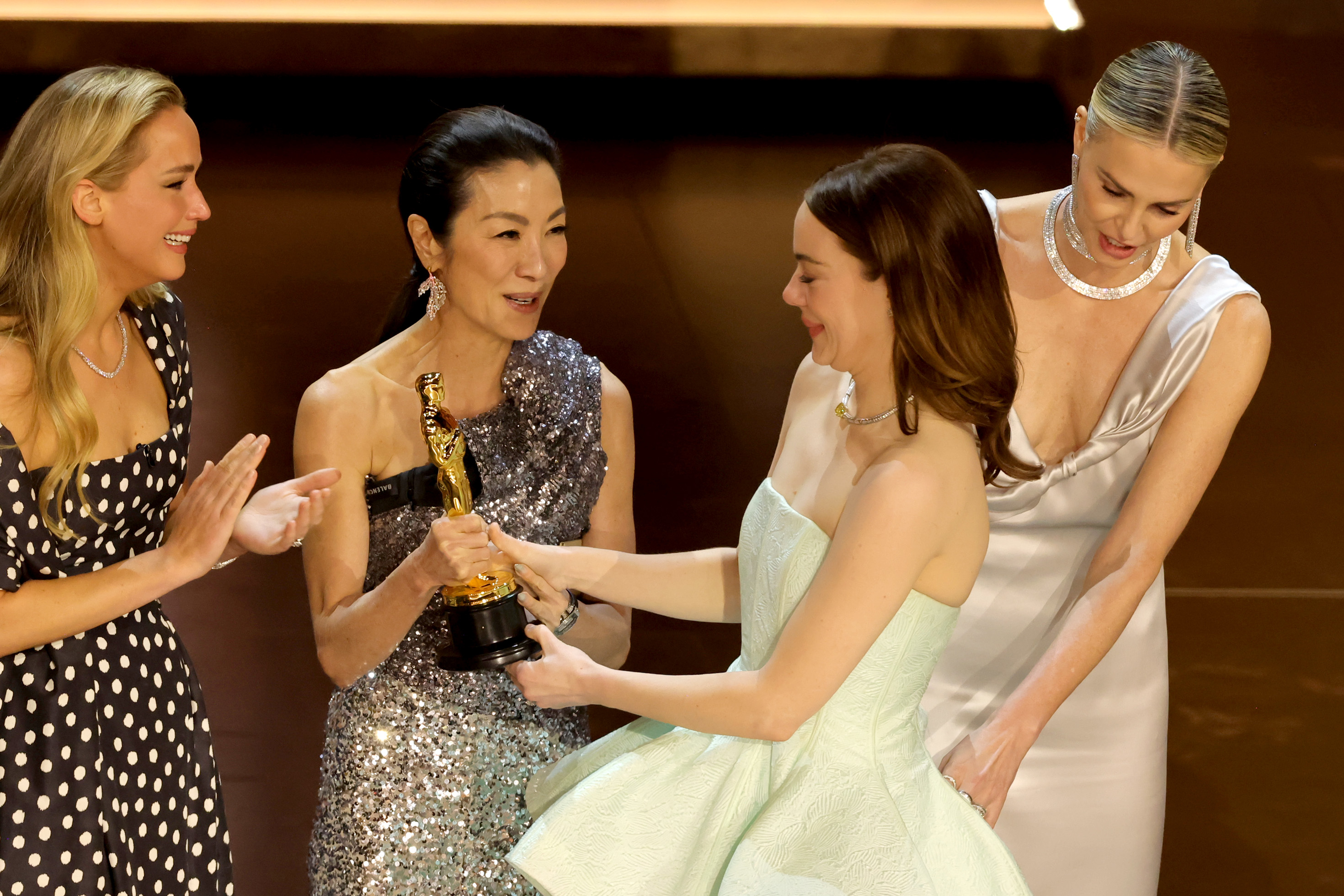 Emma with past winners, including Jennifer Lawrence and Michelle Yeoh, holding a trophy, all smiling and interacting joyfully