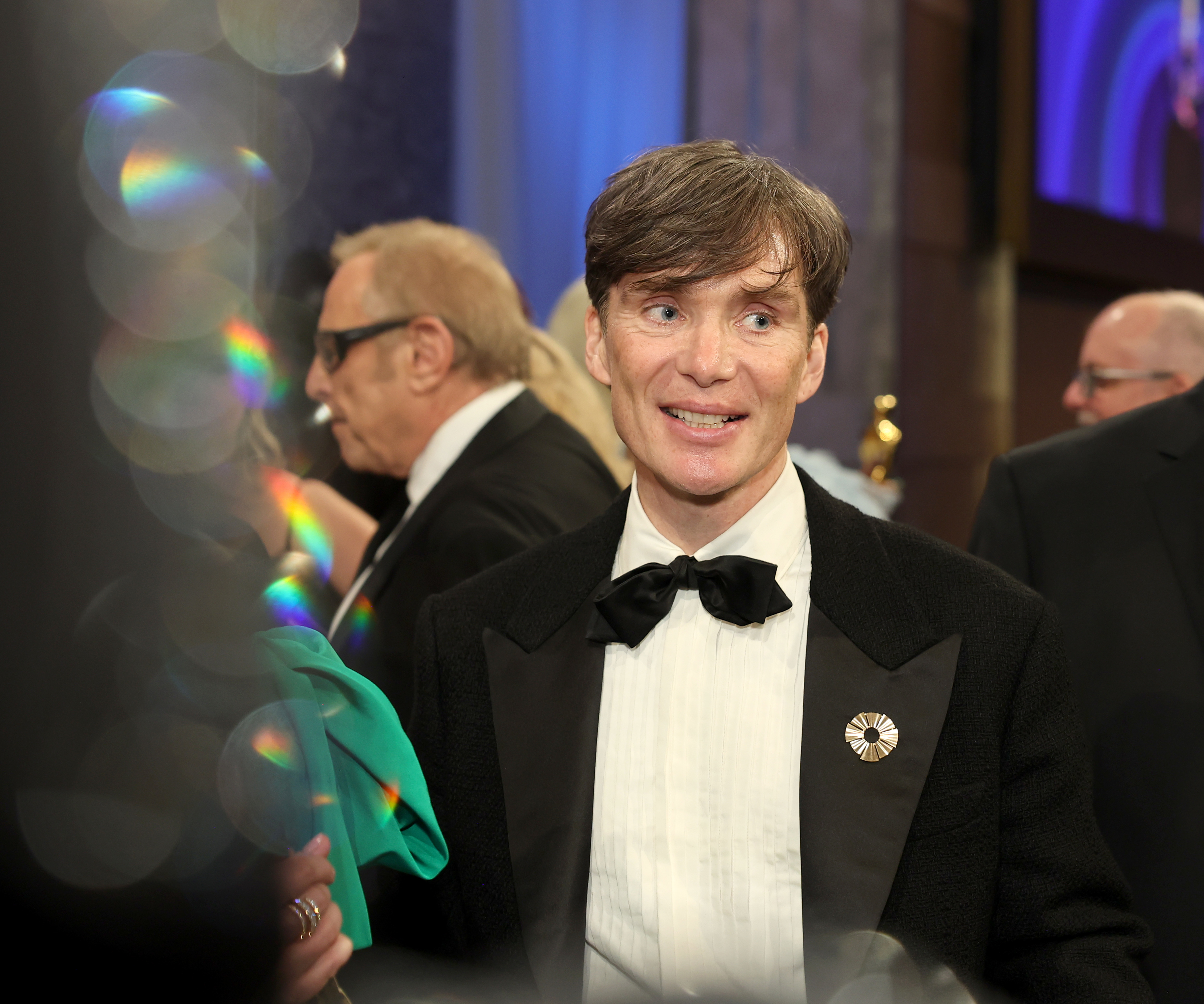 Cillian smiling in a formal suit with a bow tie and a pin on the lapel at an event