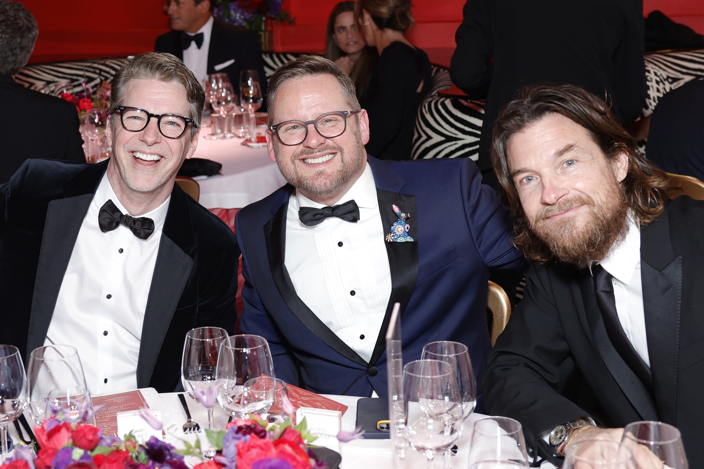 Jason Bateman, Sean Hayes, and another man in tuxedos seated at a table, smiling