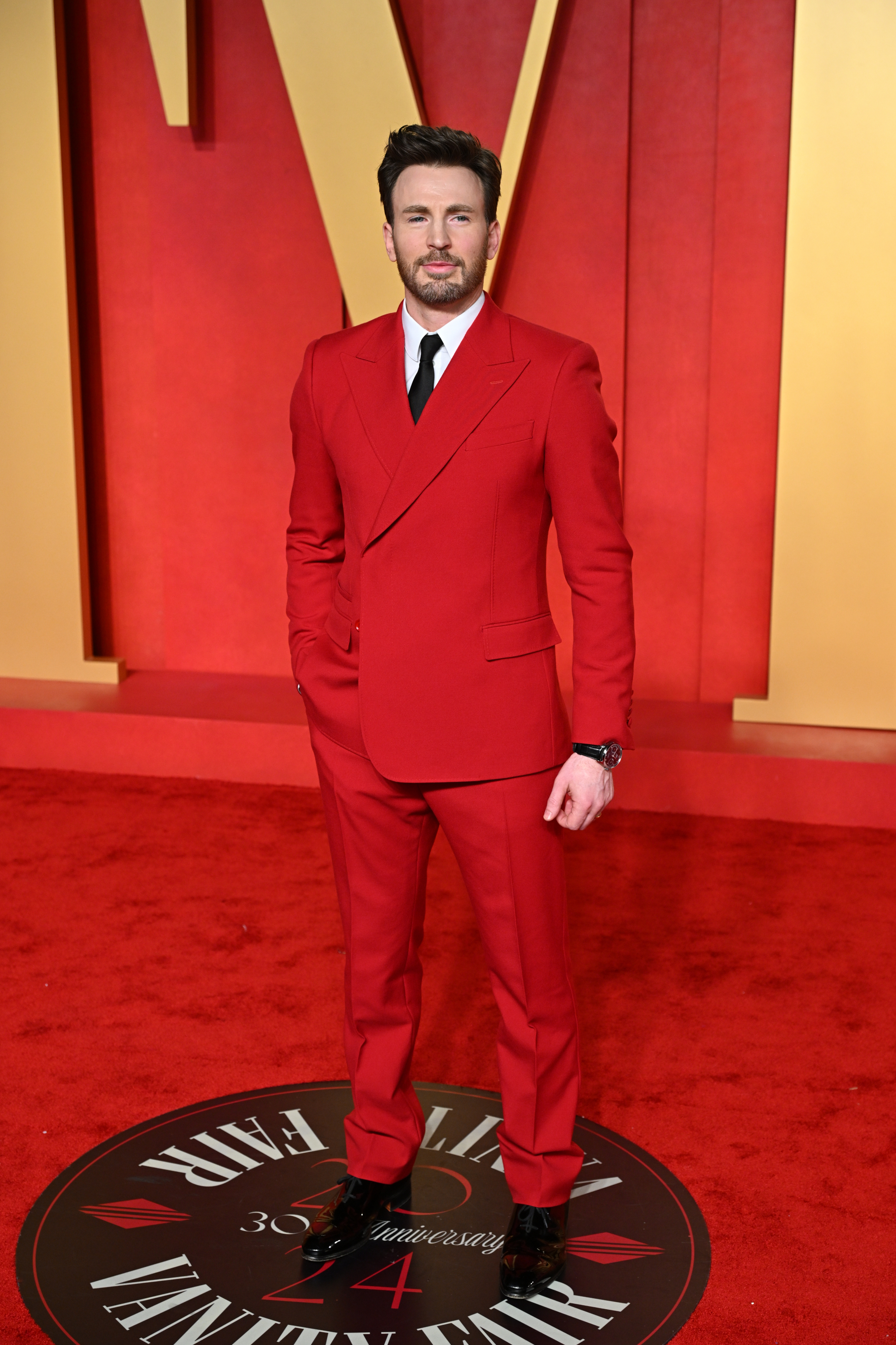 Chris in a tailored red suit standing on event carpet