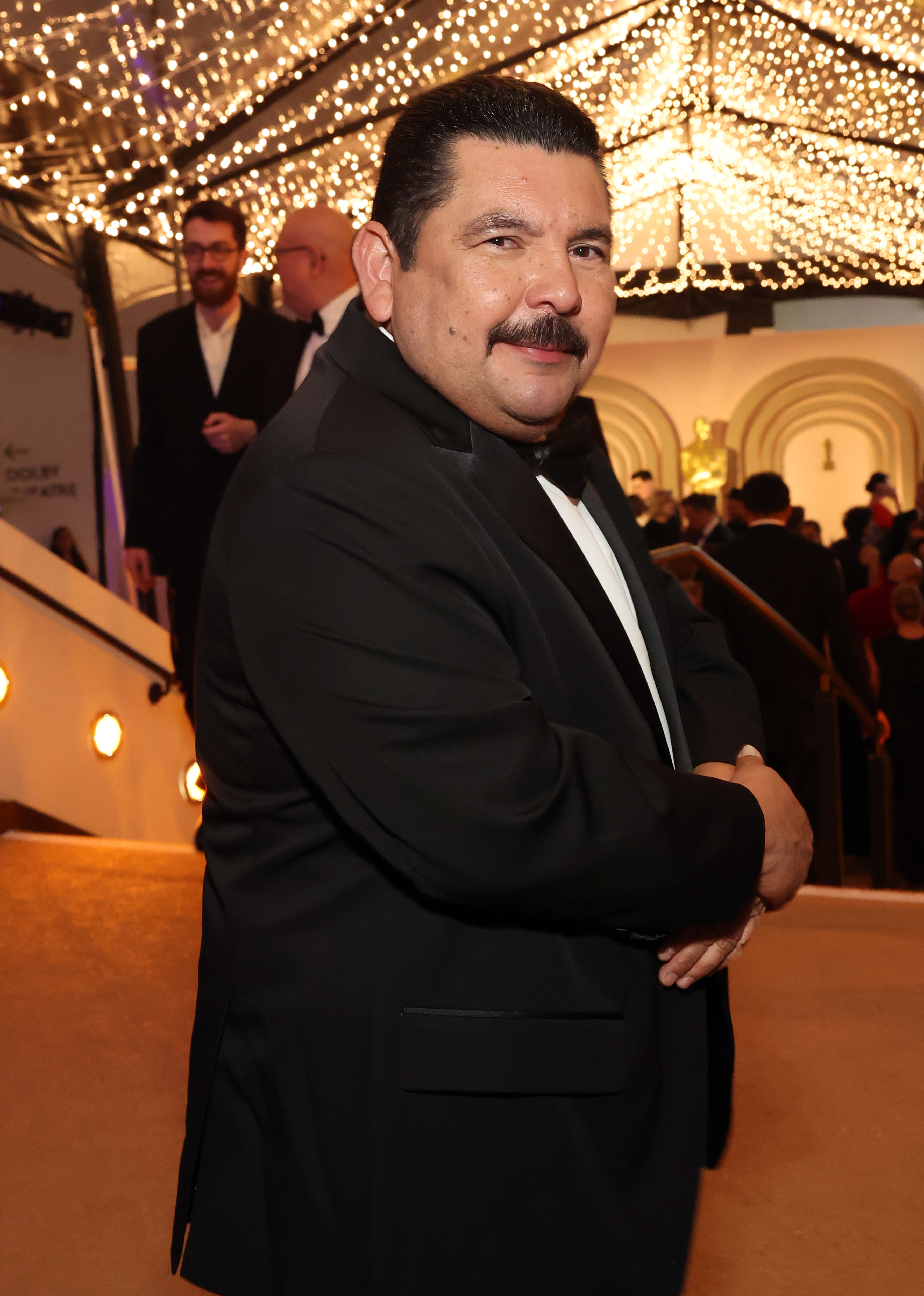 Guillermo Rodriguez from Jimmy Kimmel Live in a suit with bow-tie, arms crossed, smiling