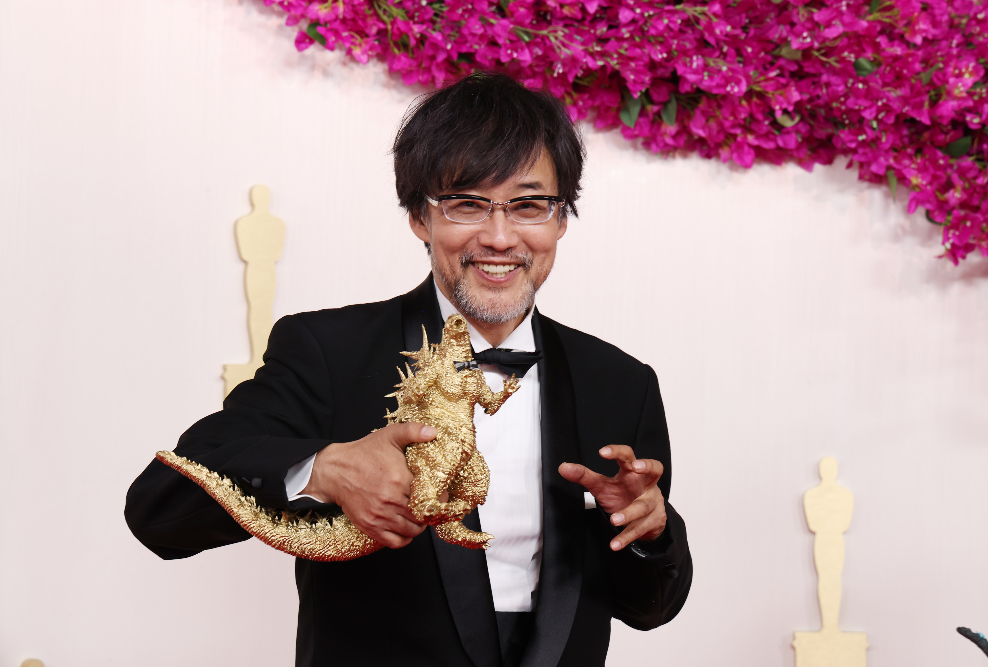 Takashi Yamazaki posing and smililng with a Godzilla toy on the Oscars red carpet