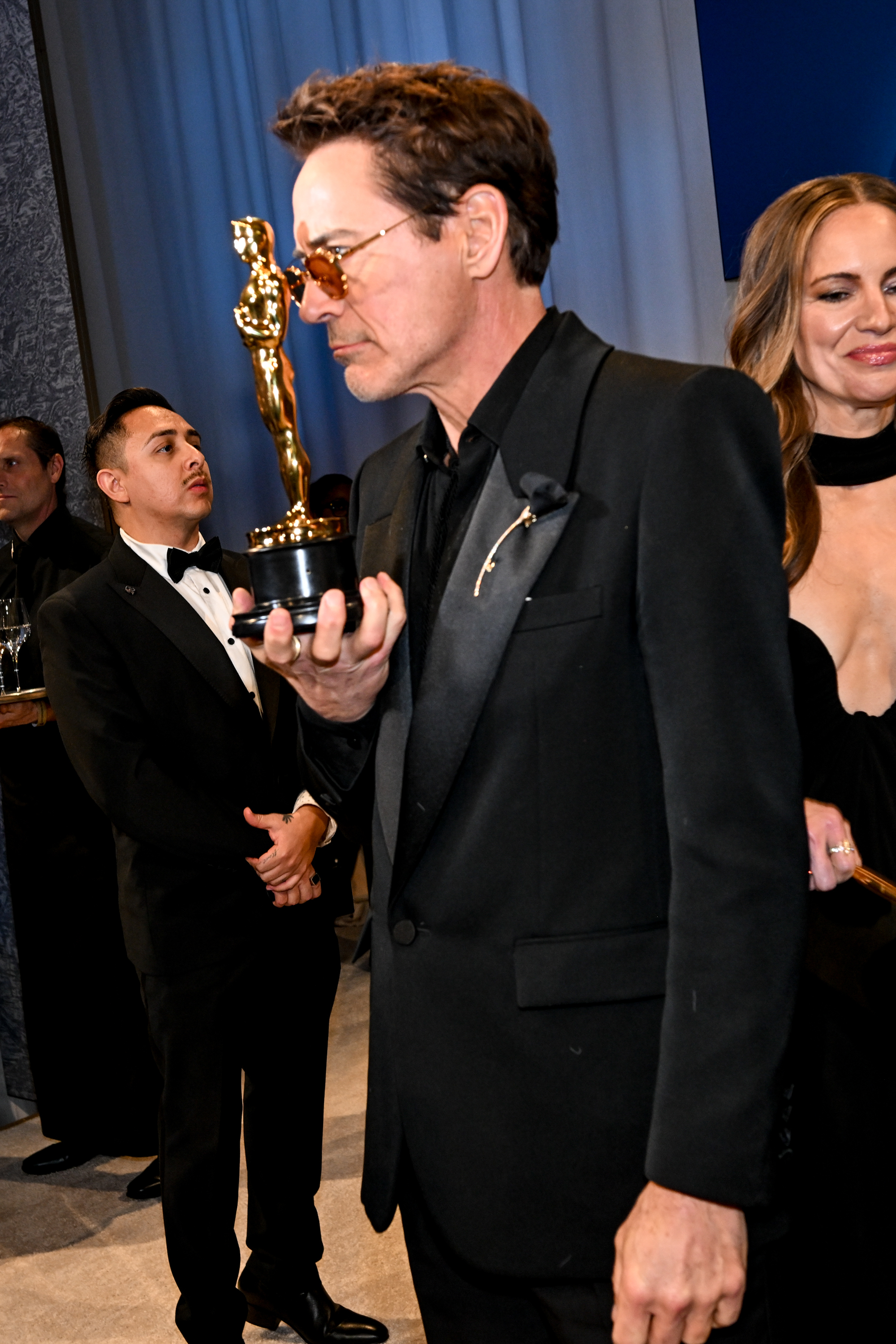 RDJ in a suit holding an Oscar close to his face with other people around him