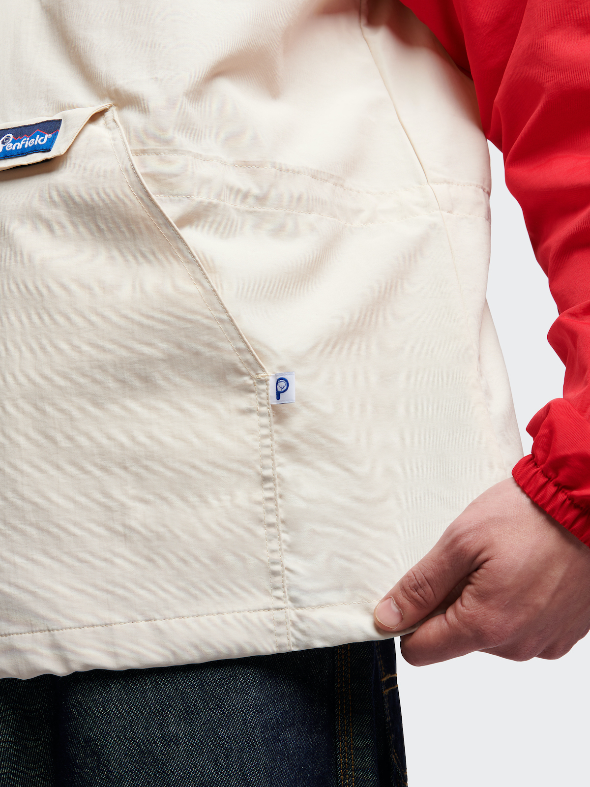 Close-up of a person modeling a beige shirt with a pocket, layered with a red sleeve, emphasizing minimal style