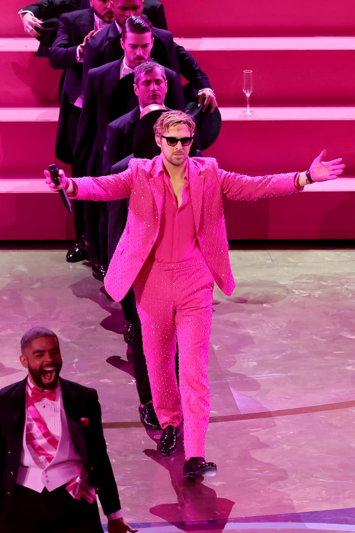 Ryan in sparkling suit with arms outstretched on stage, performers in background