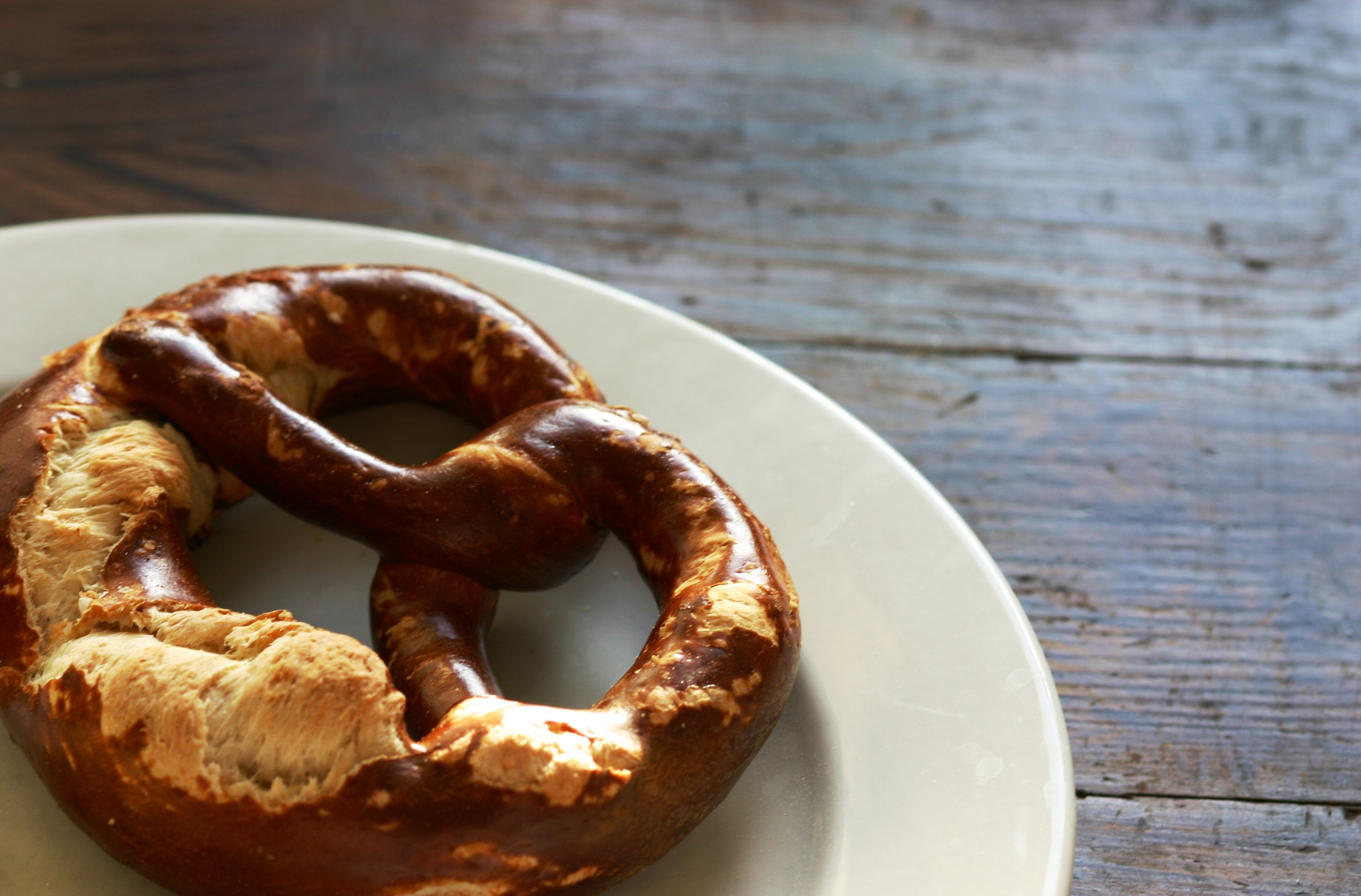 A freshly baked pretzel on a white plate with a wooden table background