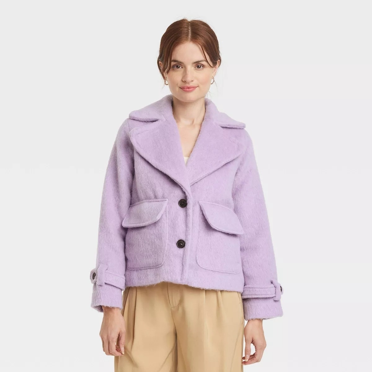 Model in a purple jacket with large buttons and flap pockets, paired with light trousers