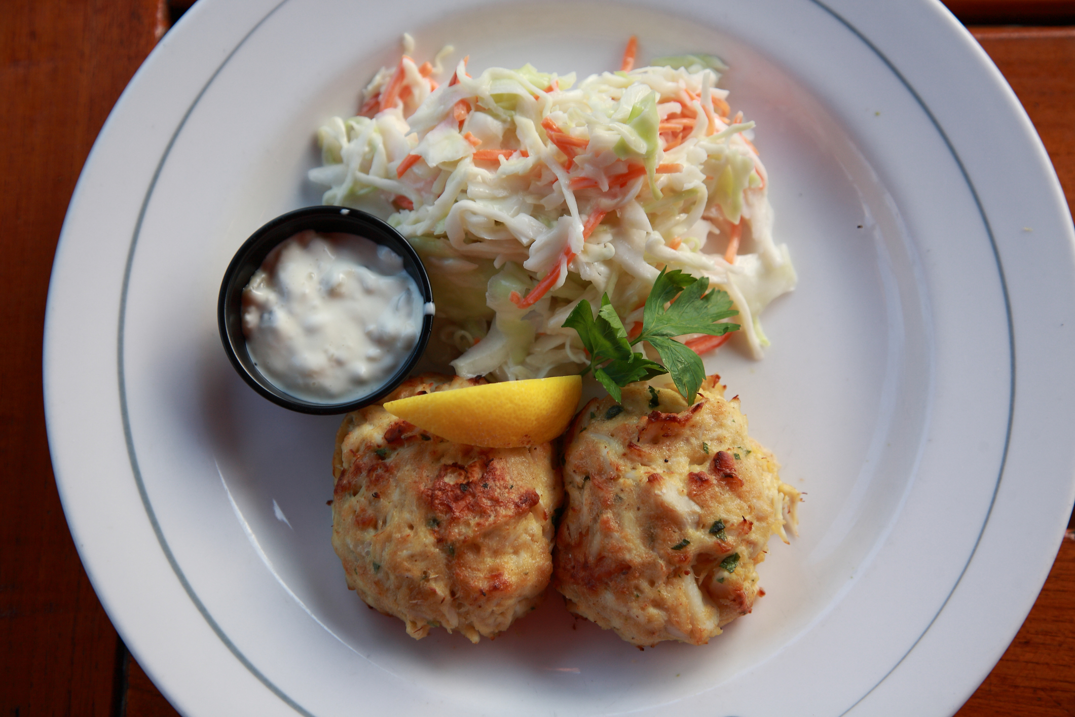 Plate with two crab cakes, a lemon wedge, coleslaw, and a side of sauce