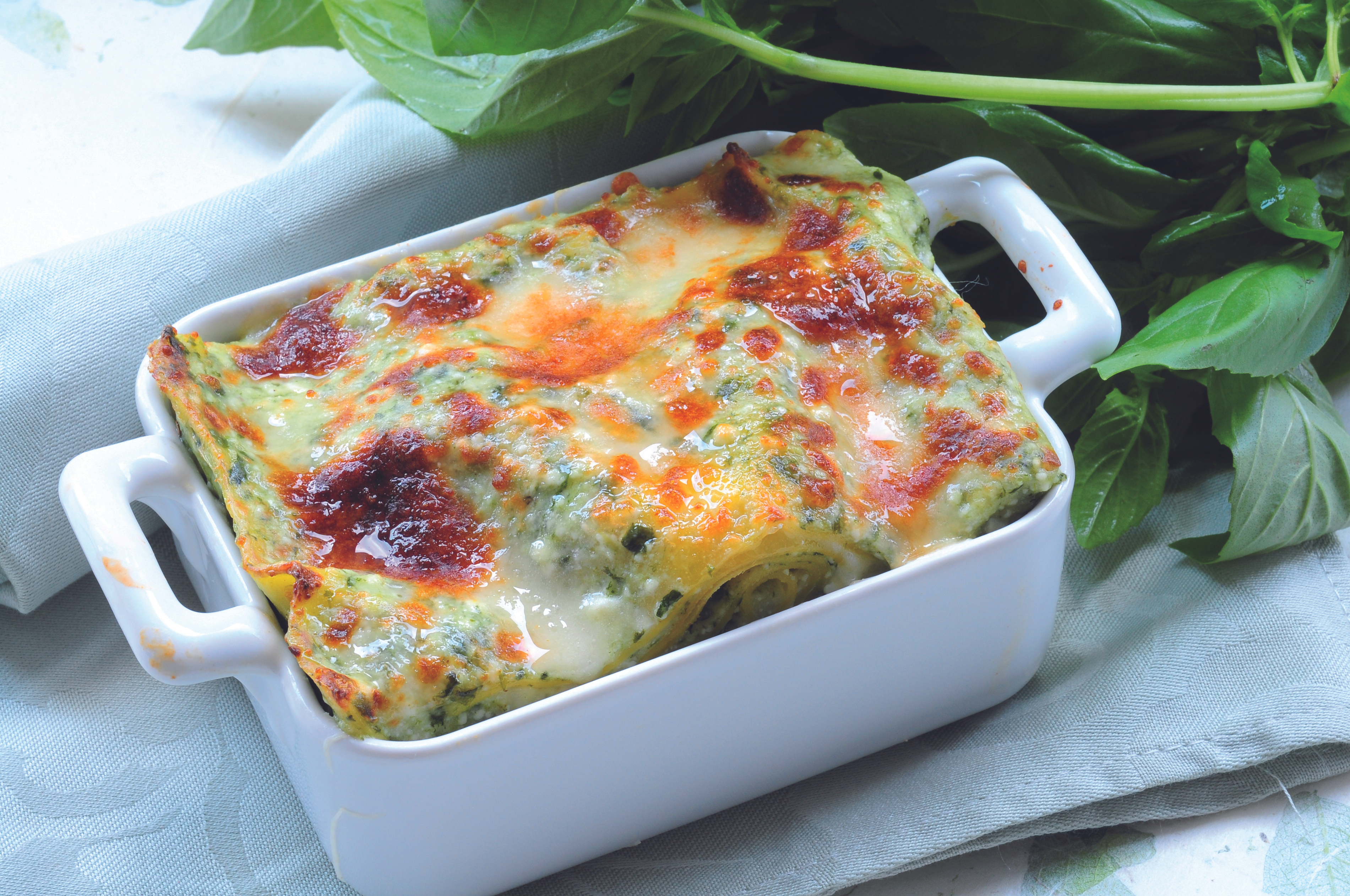 Baked spinach and cheese dish in a white ceramic container, fresh basil leaves beside it