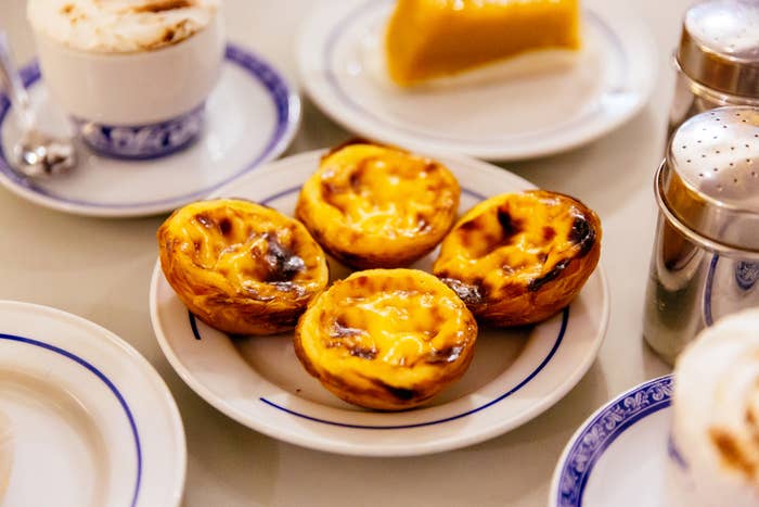 Plate with four custard tarts, cup of coffee, and a slice of cake on a table