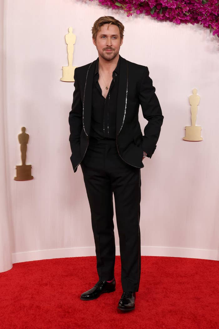 Ryan wears a suit sans tie with sequined lapels as he stands on the red carpet with his hands in his pockets