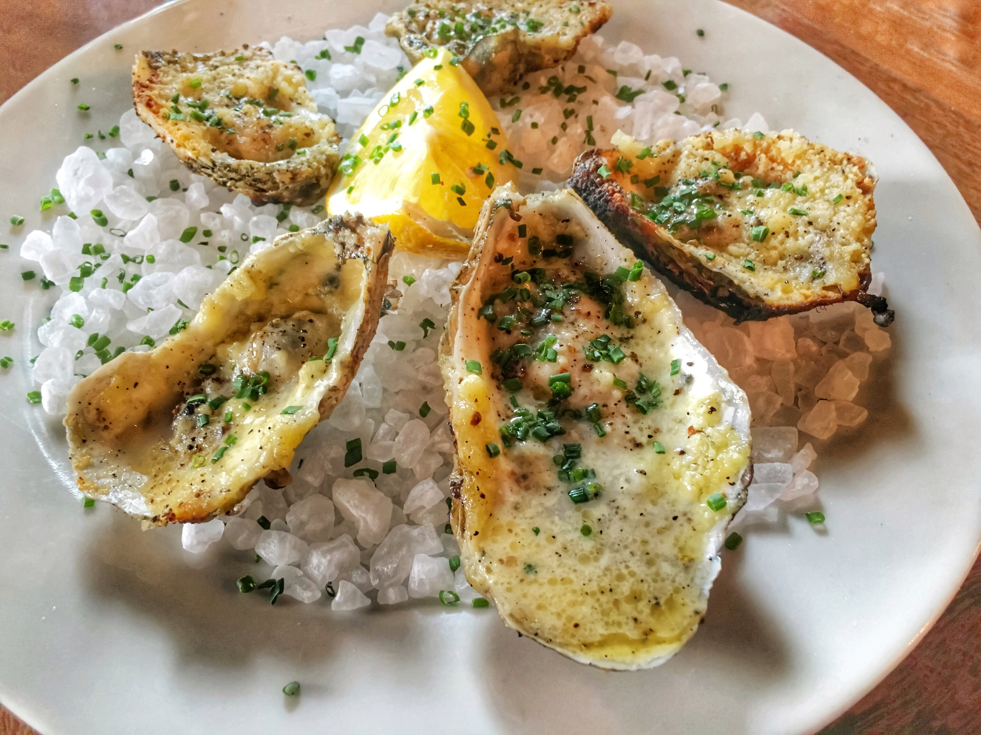 Grilled oysters on a bed of rock salt with lemon wedge and parsley on a plate